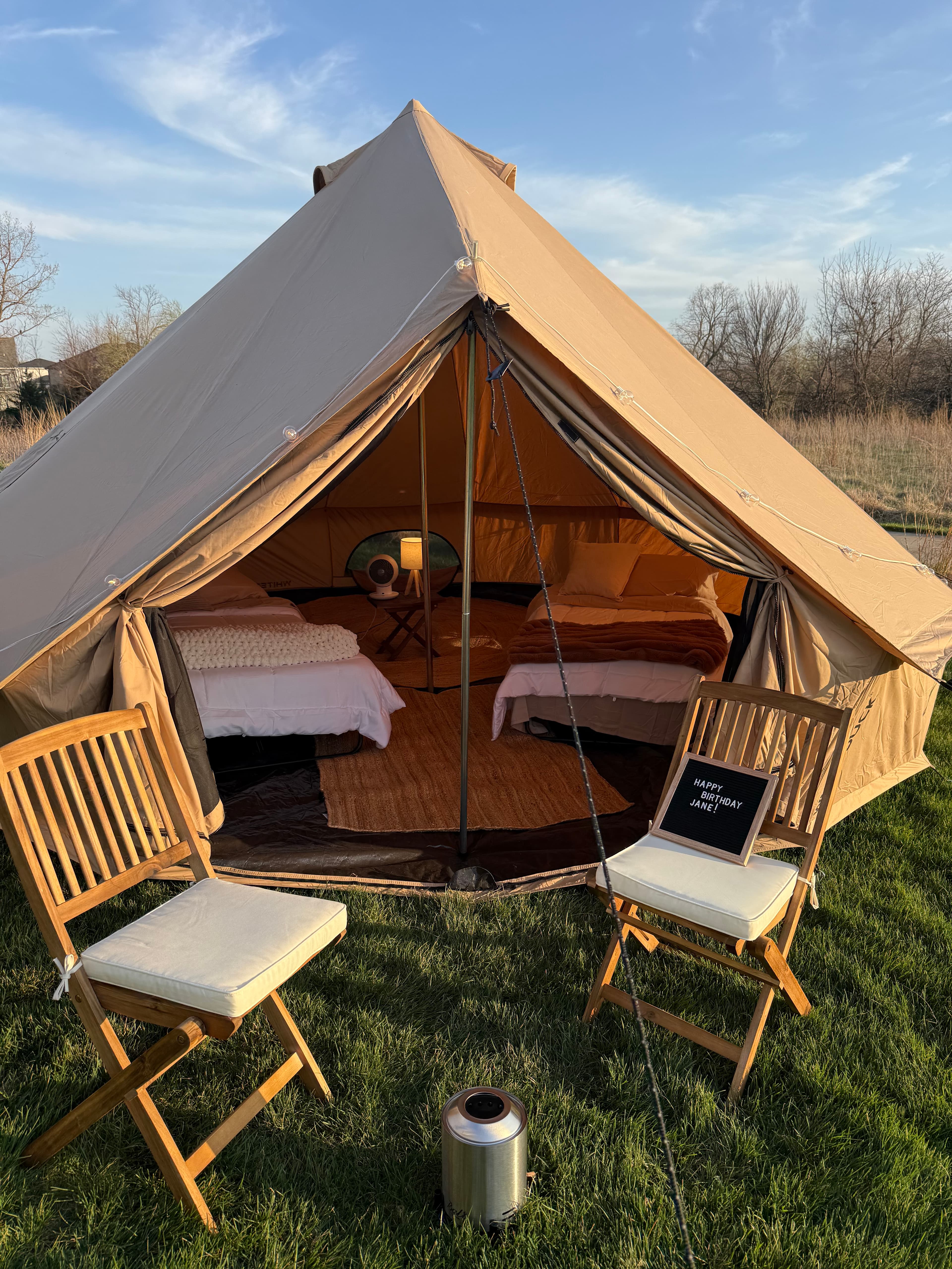 Bell tent set up at golden hour with chairs and fire pit
