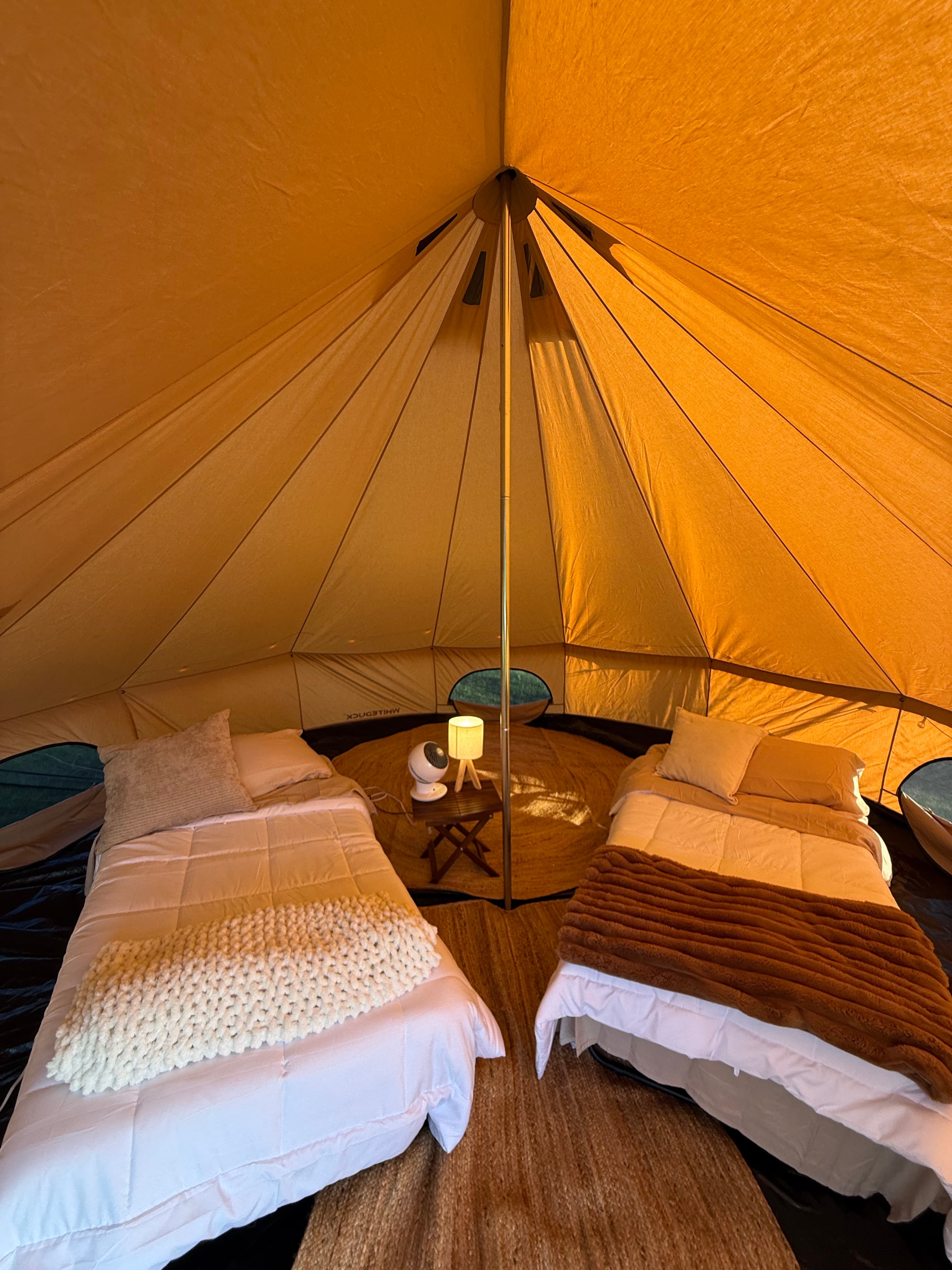 Cozy bell tent interior with bedding, pillows, and ambient lantern